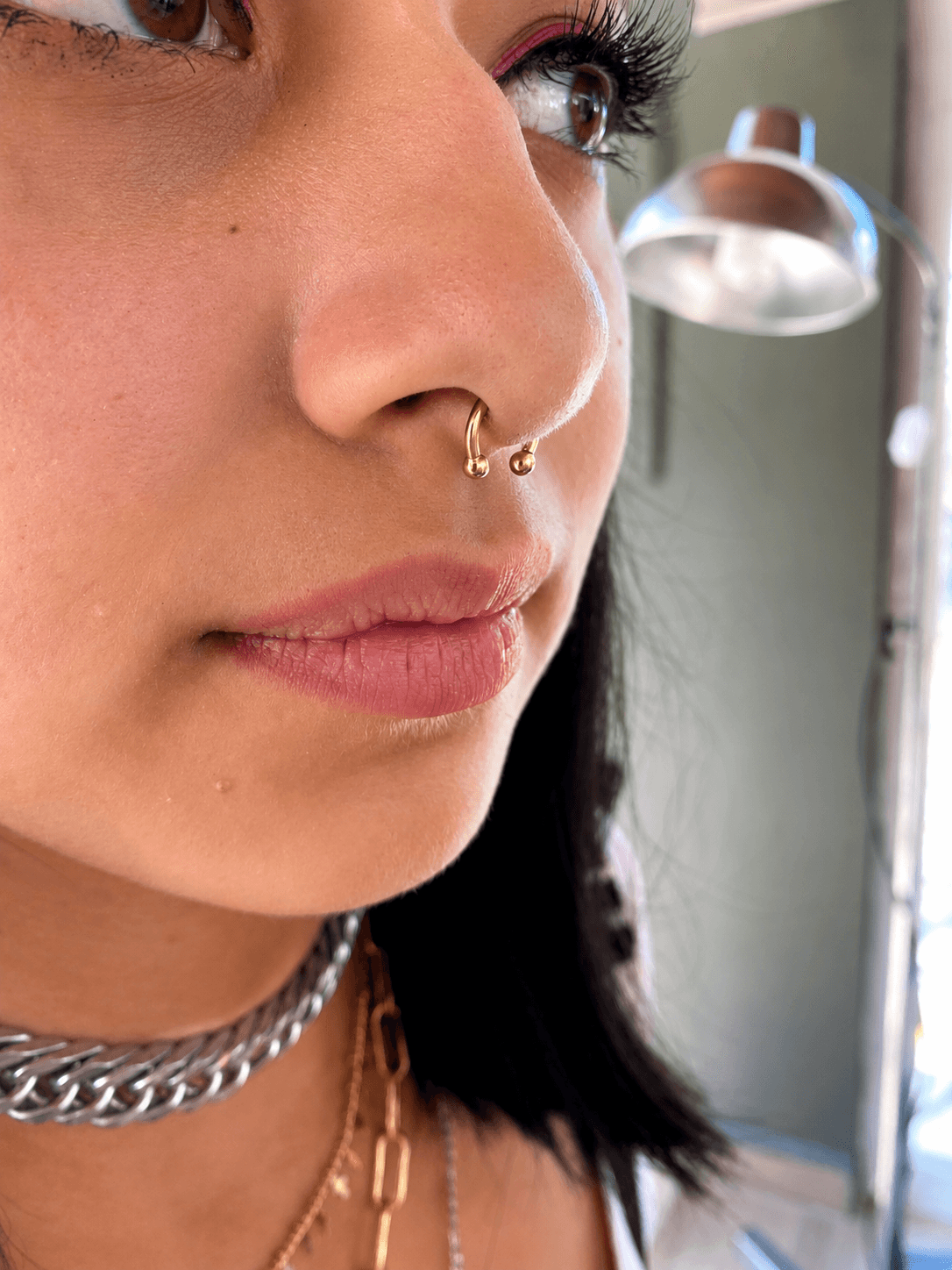Piercing septum con joyería dorada realizado por Mambas